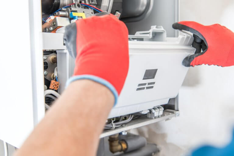 A technician in red gloves and a blue shirt is repairing a gas boiler. Expert furnace installation and repair services in Canoga Park.