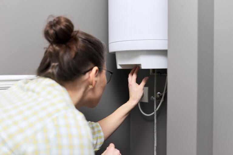 Woman adjusting temperature on electric water heater.
